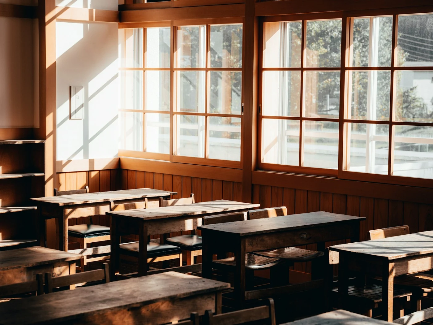 Leerer Klassenraum mit Holztischen und großen Fenstern