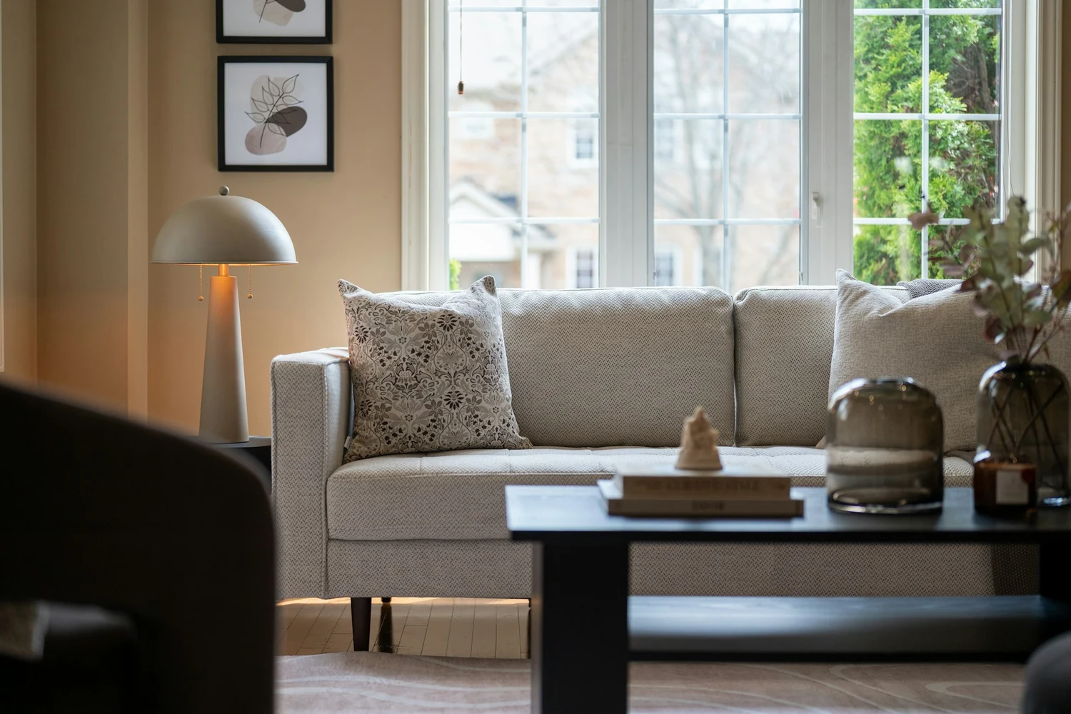 Beżowa sofa w jasnym salonie z dużym oknem