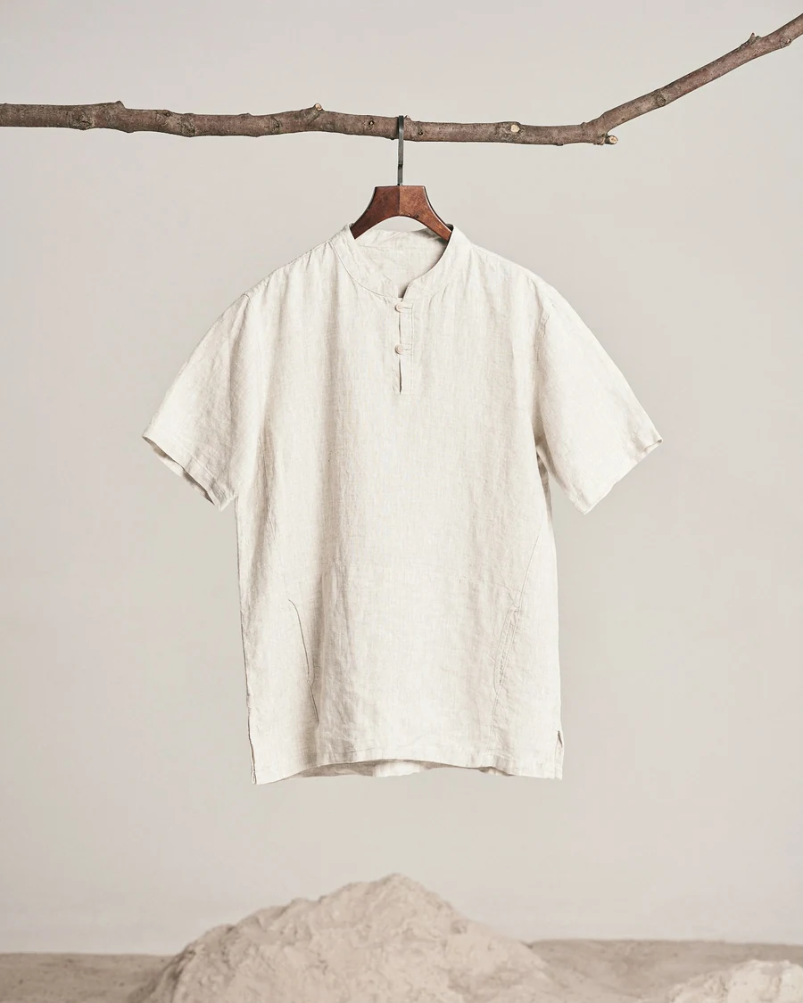 A chalk-white short-sleeved linen shirt with a henley placket hanging from a branch