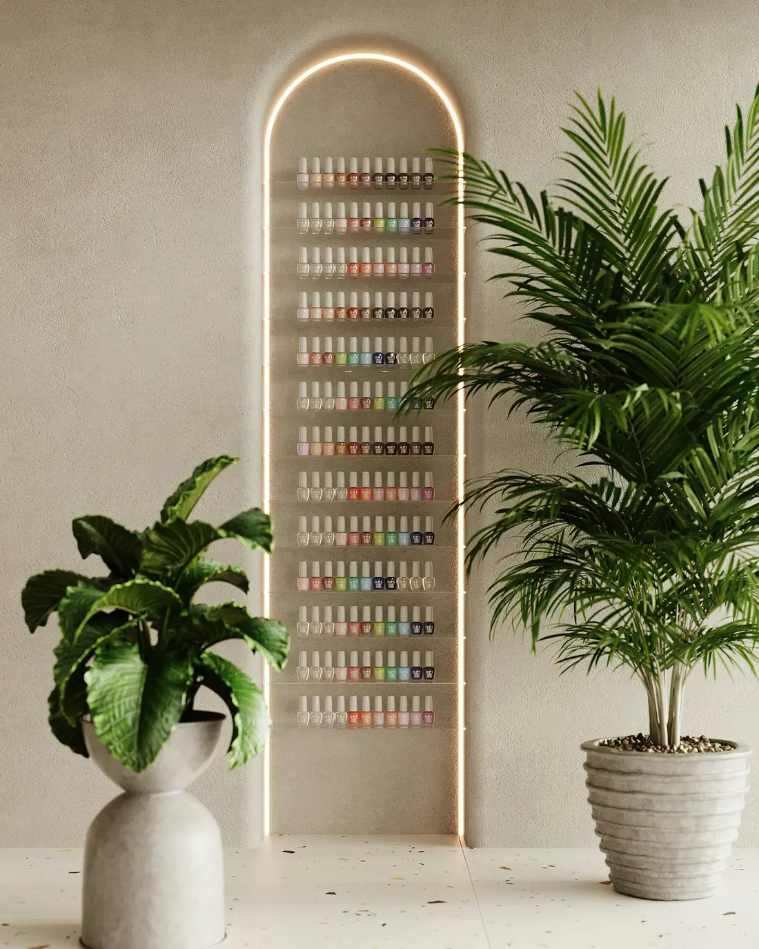 Pared del salón con esmaltes de uñas ordenados bajo un arco de luz, junto a dos plantas grandes